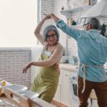 Playful senior couple in aprons dancing and smiling while preparing healthy dinner at home