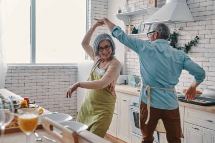 Playful senior couple in aprons dancing and smiling while preparing healthy dinner at home