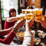 Group of young friends toasting each other with beers in a pub