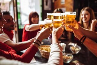 Group of young friends toasting each other with beers in a pub