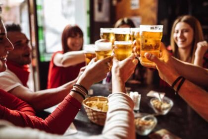 Group of young friends toasting each other with beers in a pub