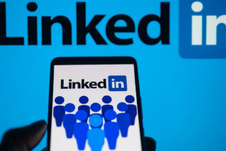 LinkedIn logo displayed on a smartphone with LinkedIn on screen seen in the background, in this photo illustration.