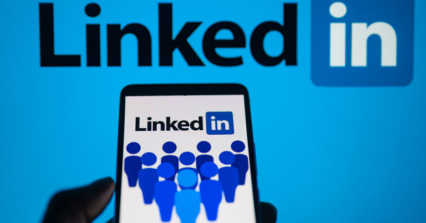 LinkedIn logo displayed on a smartphone with LinkedIn on screen seen in the background, in this photo illustration.