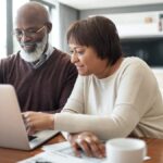 happy senior couple using a laptop in their living room to look at their financial budgets