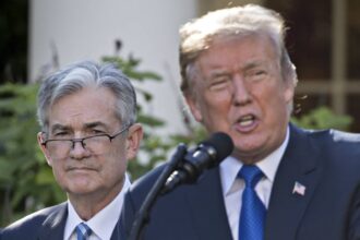 Federal Reserve Chair Jerome Powell standing behind President Donald Trump.